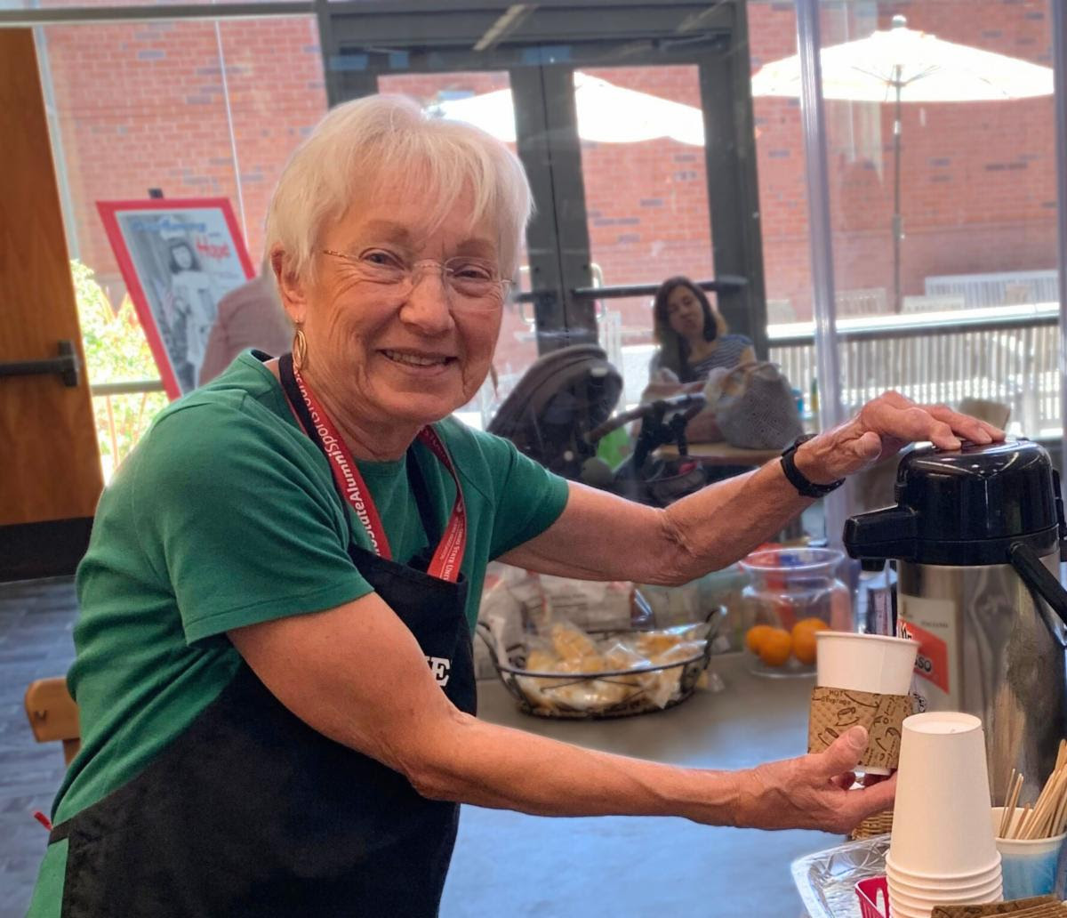 A volunteer at the Friends Cafe posing while preparing a beverage.
